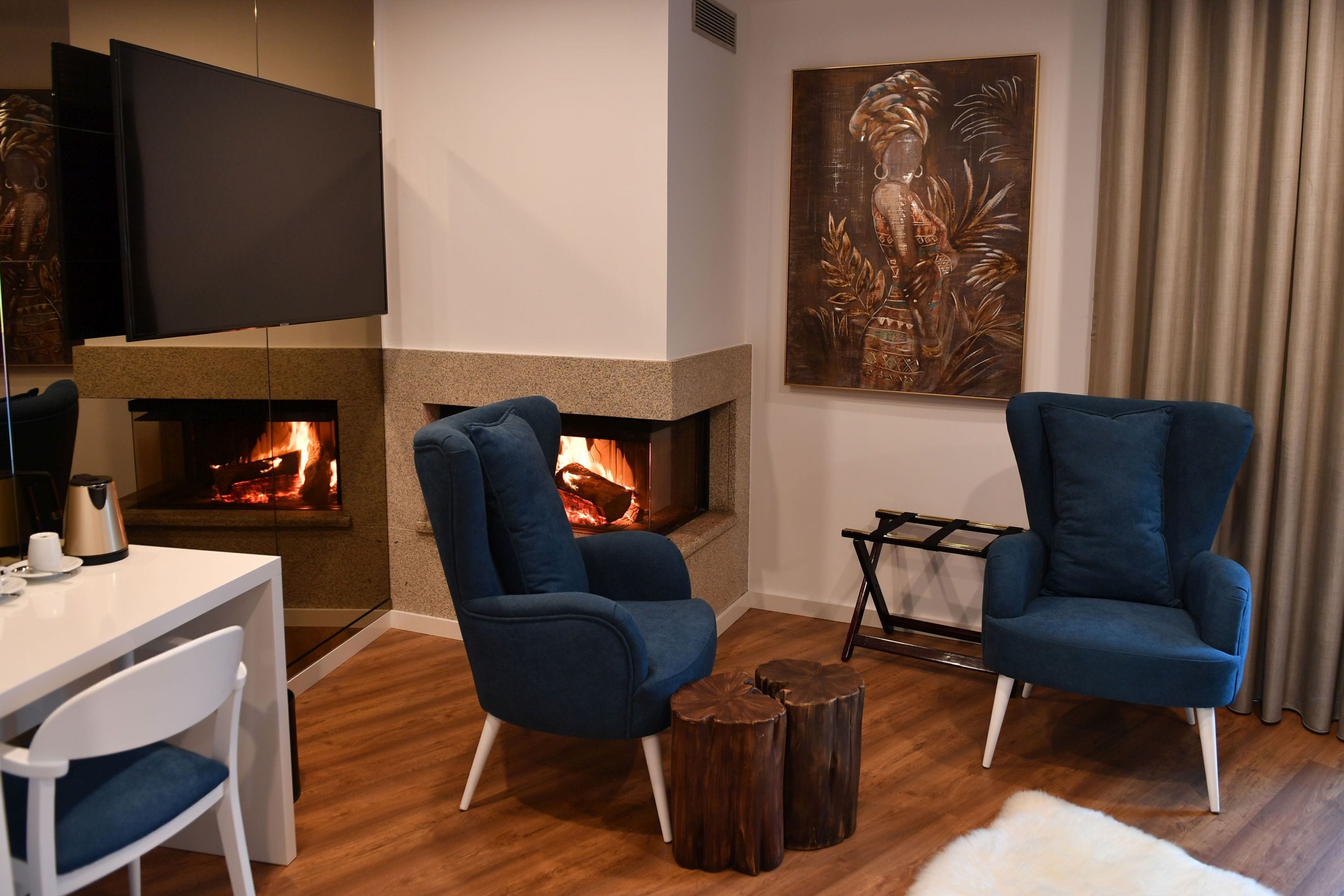 A modern living room with a fireplace, two blue armchairs, a white table, and a coffee maker.