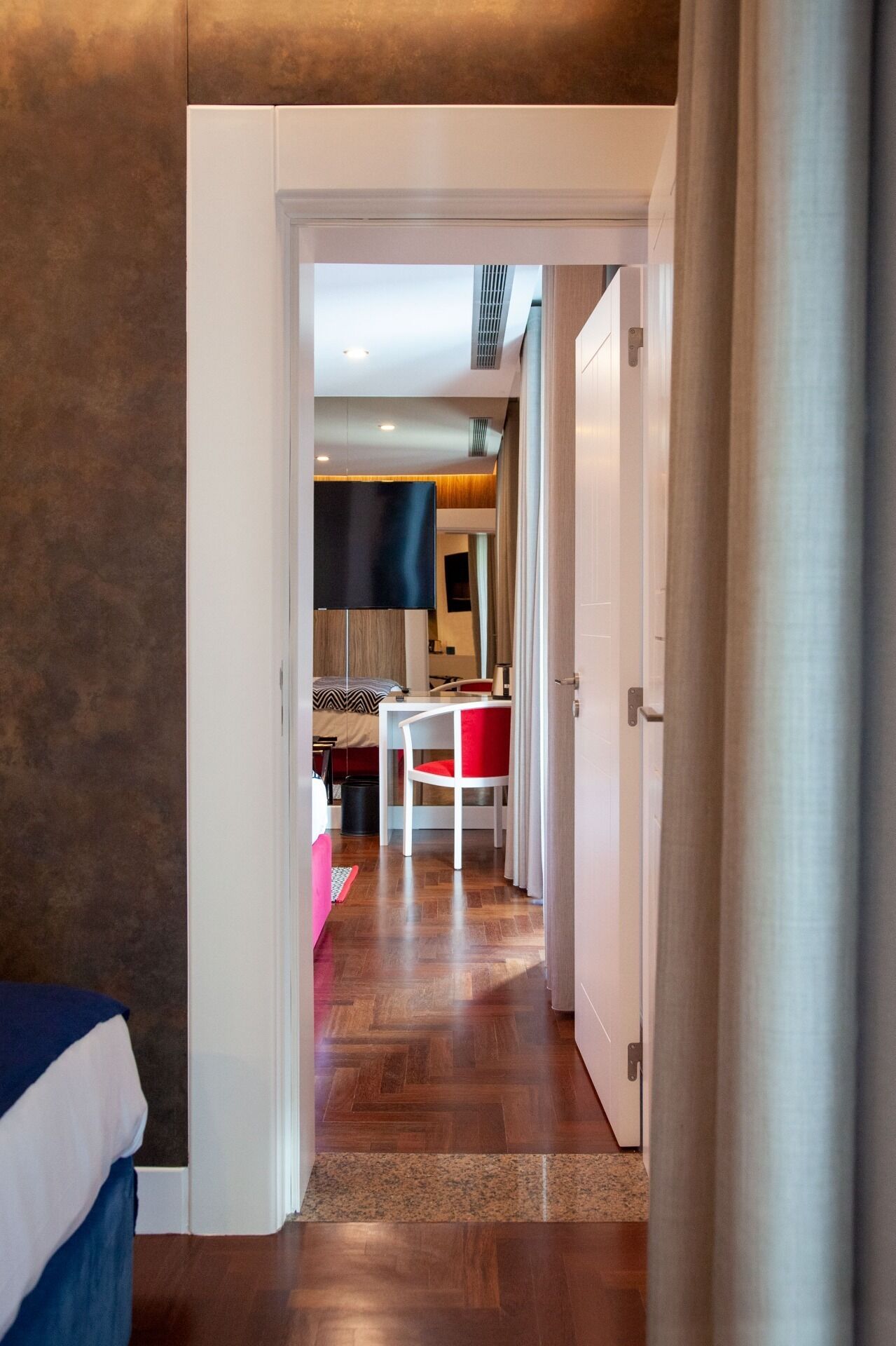 Quarto de hotel com piso de madeira, uma cama, uma mesa e uma cadeira.