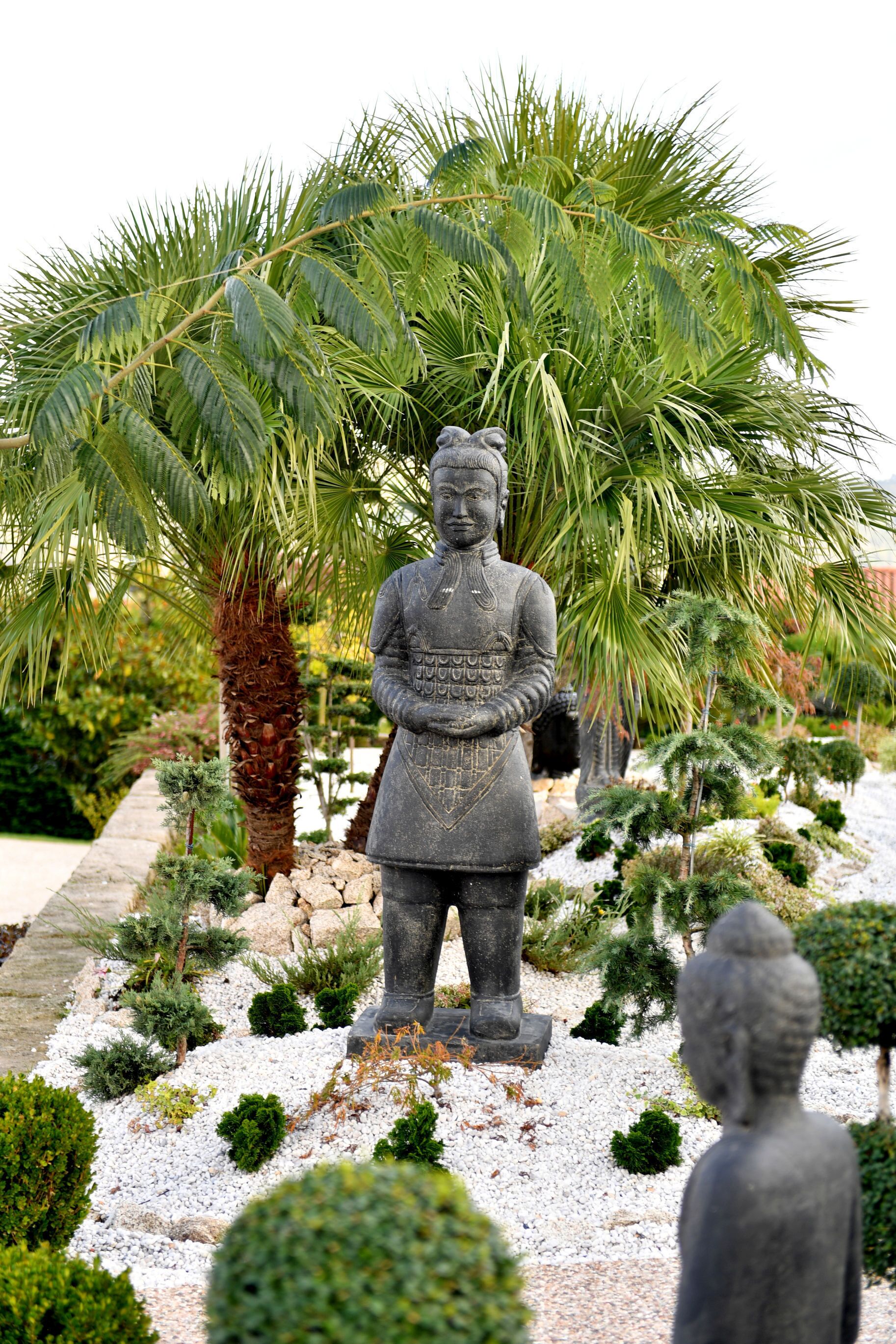 Un jardín con una estatua de una figura, palmeras y varios arbustos.