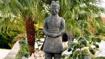 Un jardín con una estatua de una figura, palmeras y varios arbustos.