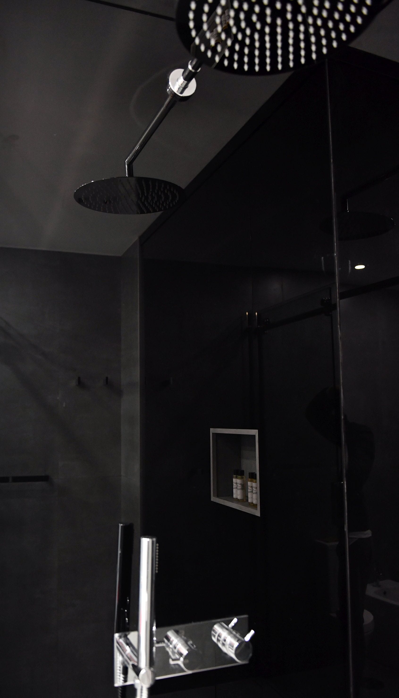 A modern bathroom with a large mirror, a shower head, and a small shelf with toiletries.