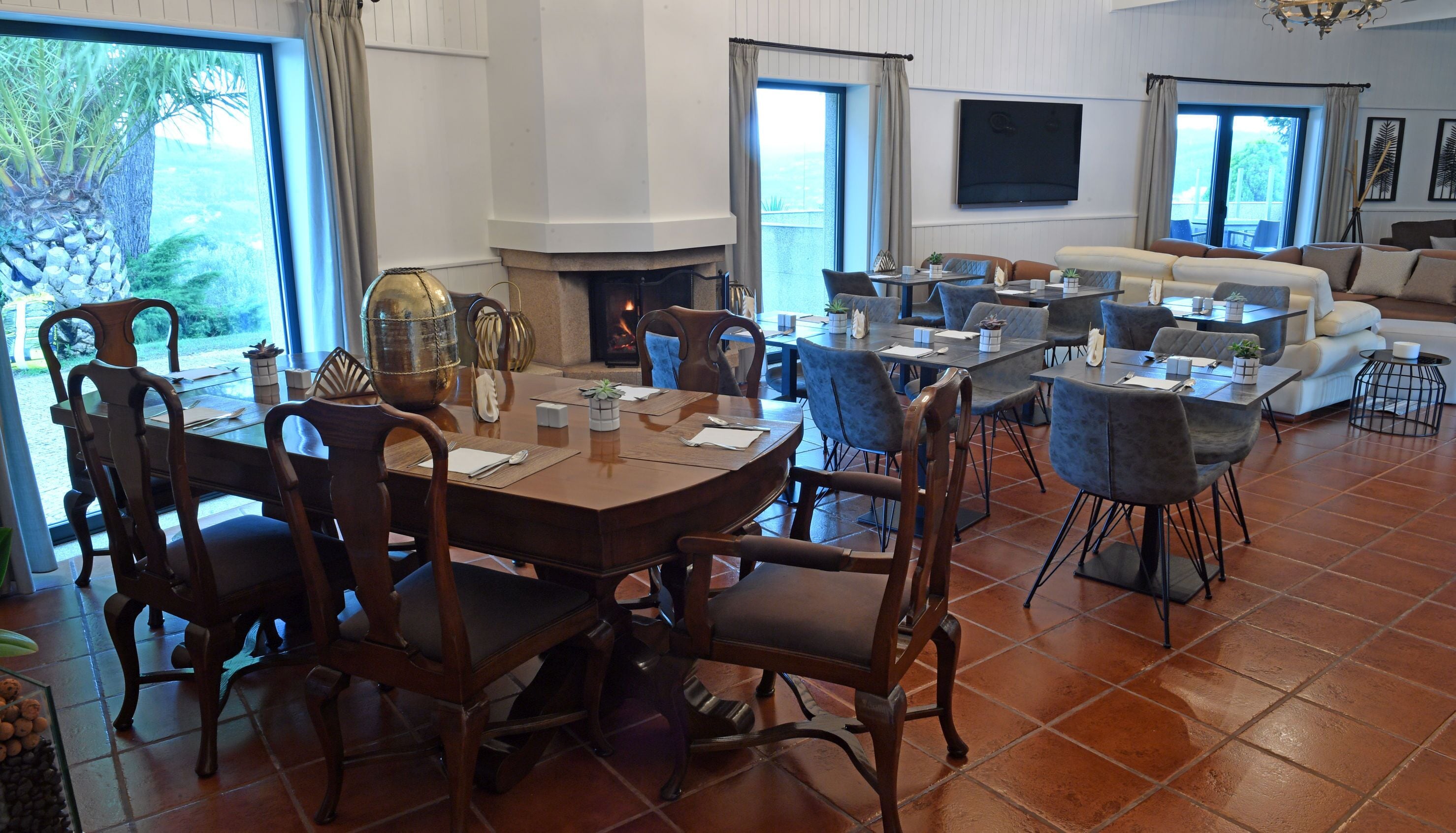 A spacious dining area with a large wooden table and chairs, a fireplace, and a living area with sofas and a TV.