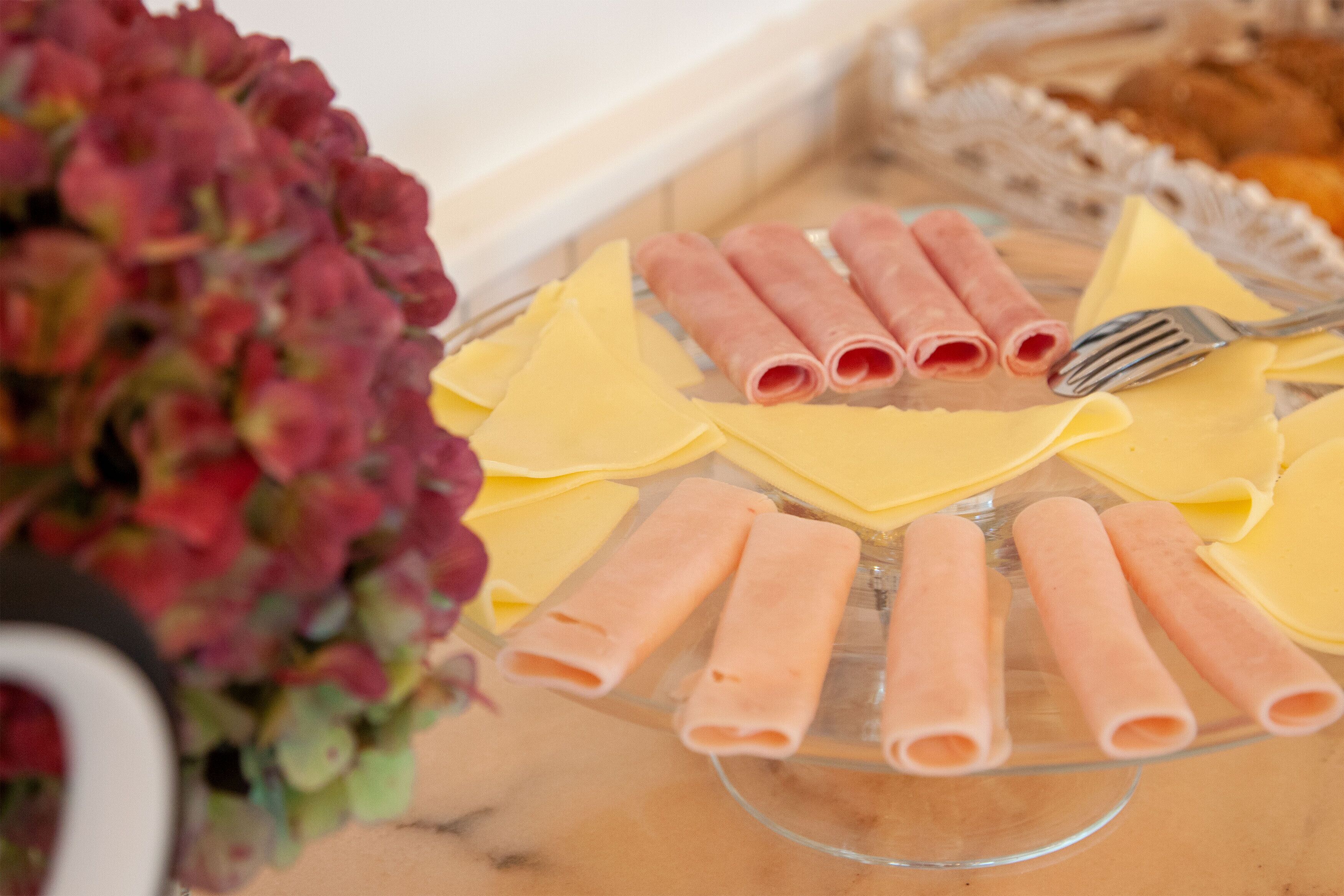 A glass serving tray with yellow cheese and pink meat rolls.