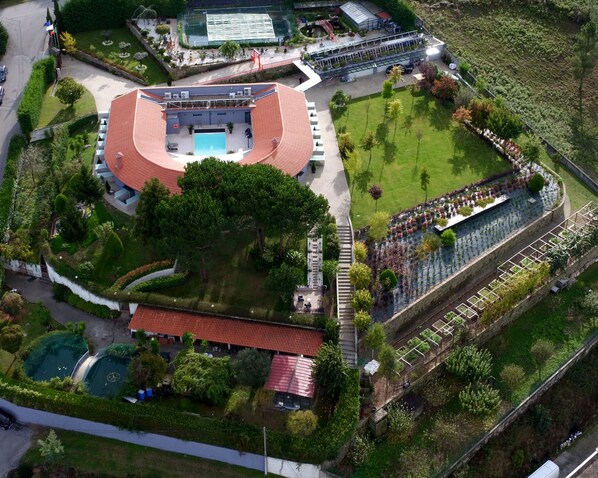 Vista aérea de un hotel con piscina, canchas de tenis e invernadero.