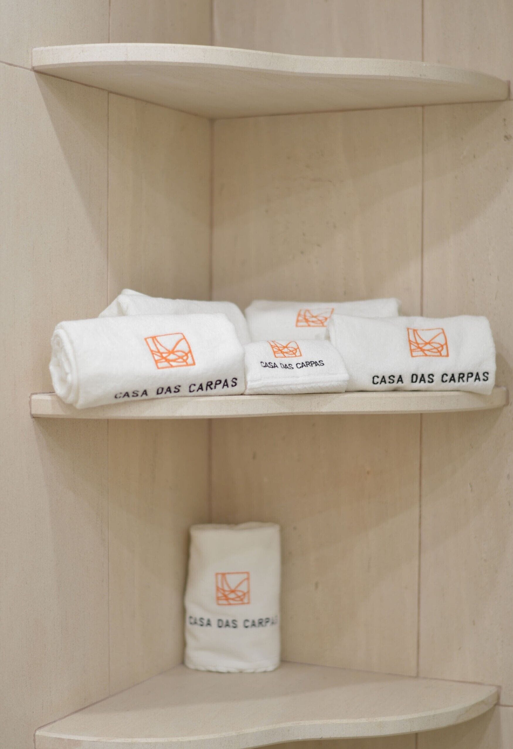 Joc de tovalloles blanques amb el distintiu de 'Casa Das Carpas' sobre una prestatgeria de fusta.