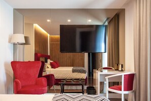 Una habitación de hotel moderna con una cama grande, un sillón rojo, un escritorio blanco y un televisor de pantalla plana.