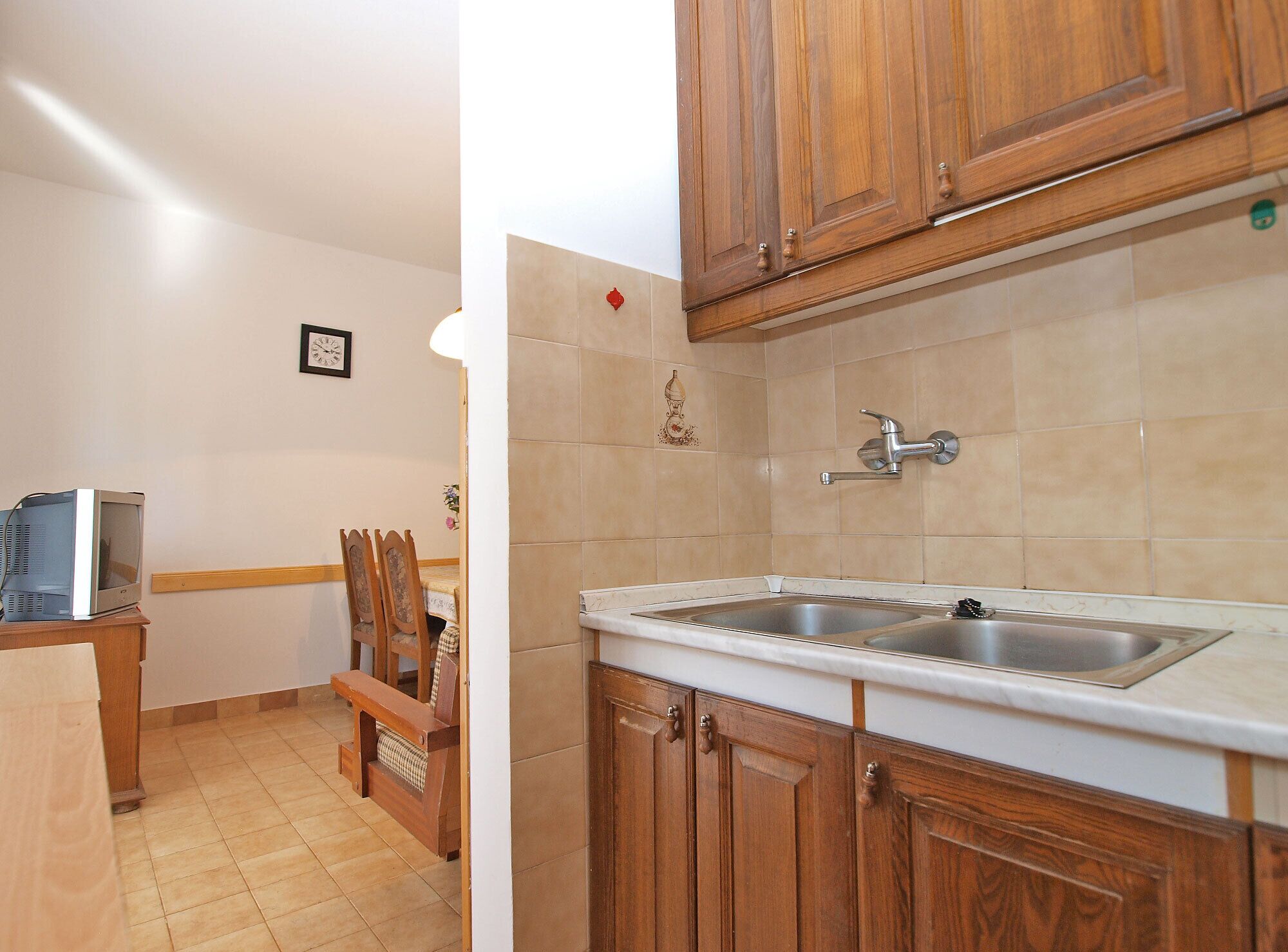 A kitchen with wooden cabinets, a double sink, and a small dining area with a bench and chairs.