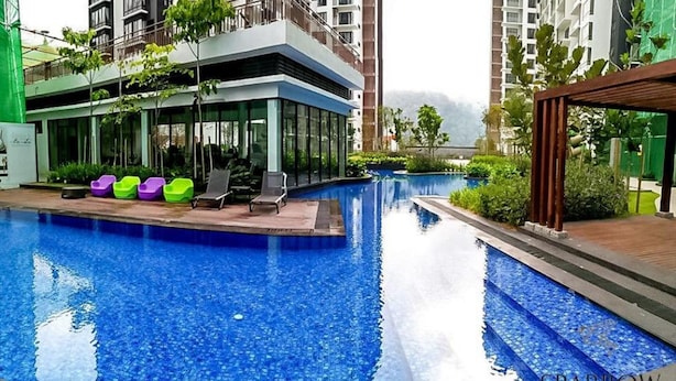 A swimming pool with lounge chairs and colorful chairs, surrounded by greenery and modern buildings. - Midhills Premium Suites by Sparrow Homes (Genting Highlands)