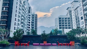 A modern building with multiple floors, outdoor seating, and a view of other high-rise buildings in the background. - Midhills Premium Suites by Sparrow Homes (Genting Highlands)