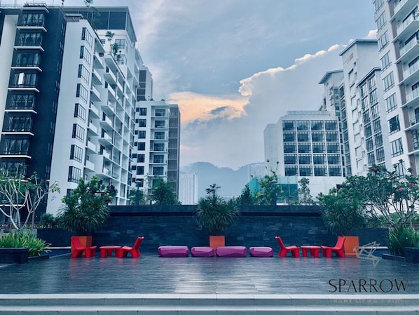 A modern building with multiple floors, outdoor seating, and a view of other high-rise buildings in the background.