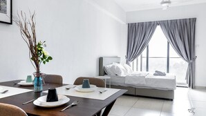 A modern hotel room with a bed, a dining area with a table and chairs, and a window with curtains. - Midhills Premium Suites by Sparrow Homes (Genting Highlands)