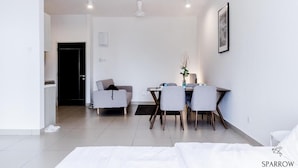 A modern, minimalist hotel room with a bed, a dining area with a table and chairs, a sofa, and a small table with a vase. - Midhills Premium Suites by Sparrow Homes (Genting Highlands)
