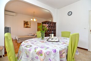 A dining area with a round table covered in a floral tablecloth, surrounded by green chairs.