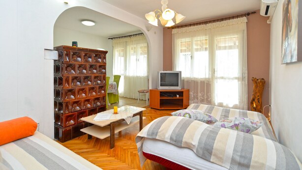 A cozy room with a bed, a wooden bookshelf, a television, and a window with curtains.