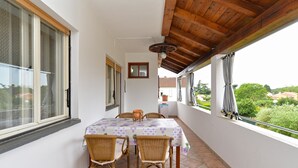 A balcony with a table and chairs, wooden ceiling, and a view of greenery and buildings.