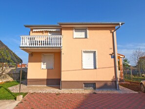 Two-story building with a flat roof and a balcony on the upper floor, featuring a small entrance and a paved walkway.