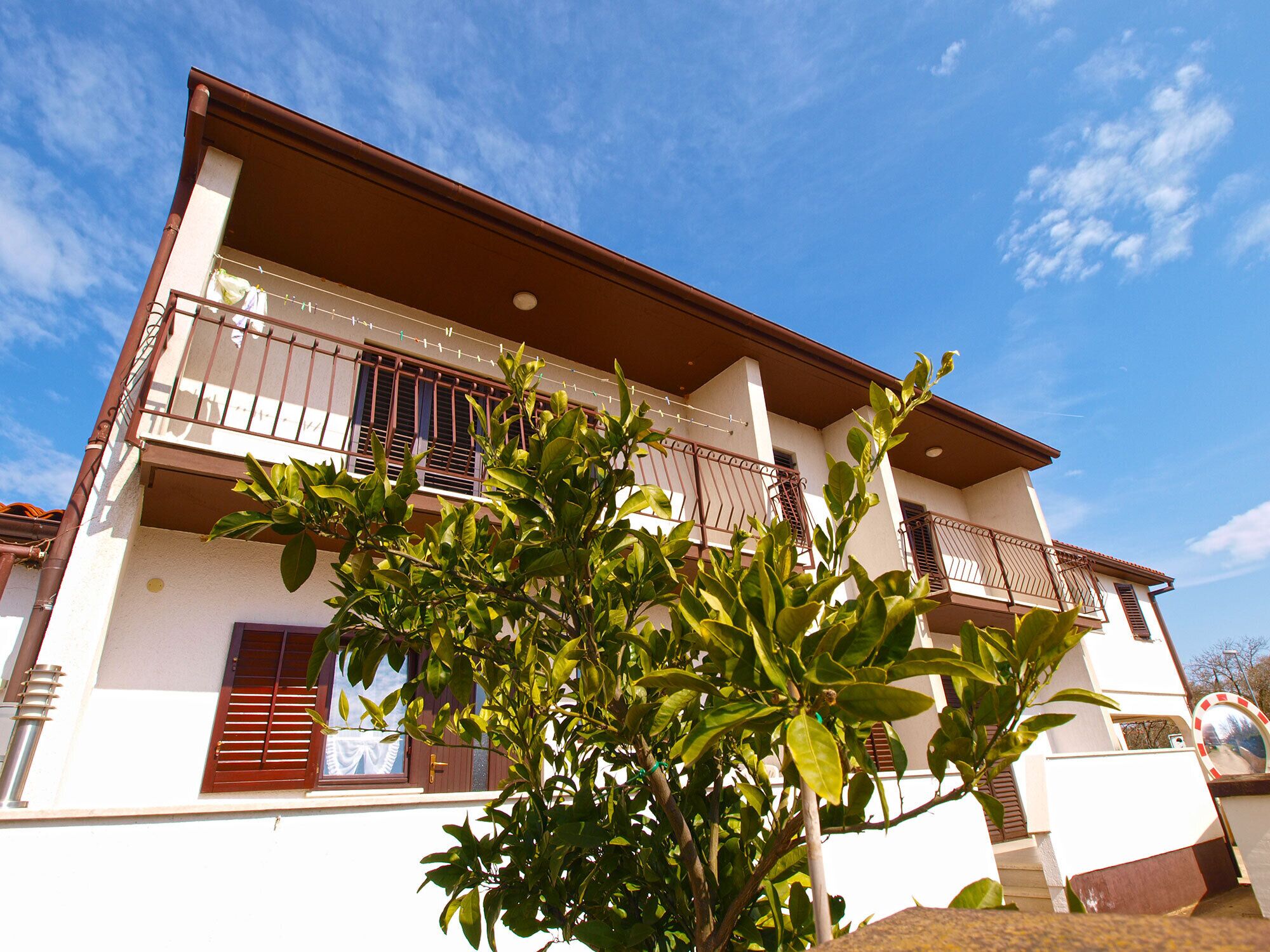 Un bâtiment à deux étages doté d’un balcon, d’une fenêtre avec des volets et d’un arbre au premier plan.