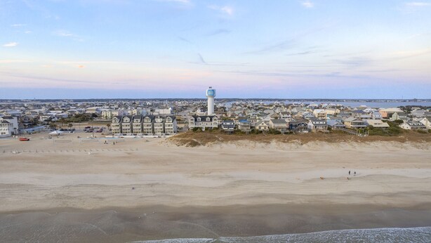 Un pueblo costero con un faro destacado, una playa de arena y edificios residenciales.