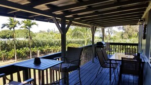Une terrasse extérieure couverte, dotée d’un plancher en bois, de rampes en métal et de meubles en osier.