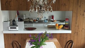 Een houten eettafel met een donkere schaal in het midden en een paarse vaas met bloemen.