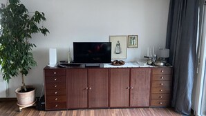Een woonkamer met een televisie, een houten kast, een plant in pot en een raam met gordijnen.
