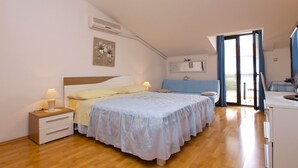 A bedroom with a bed, bedside tables, a nightstand, an air conditioning unit, a window with curtains, and a view of the outside.