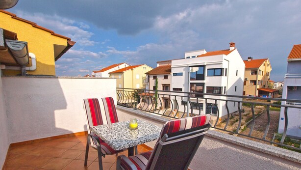 A balcony with a table and chairs, a yellow wall, and a view of residential buildings.