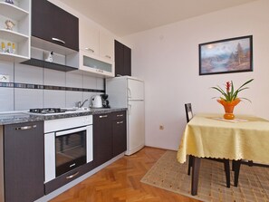 Una cocina compacta con electrodomésticos modernos, un comedor con mesa y un cuadro en la pared.