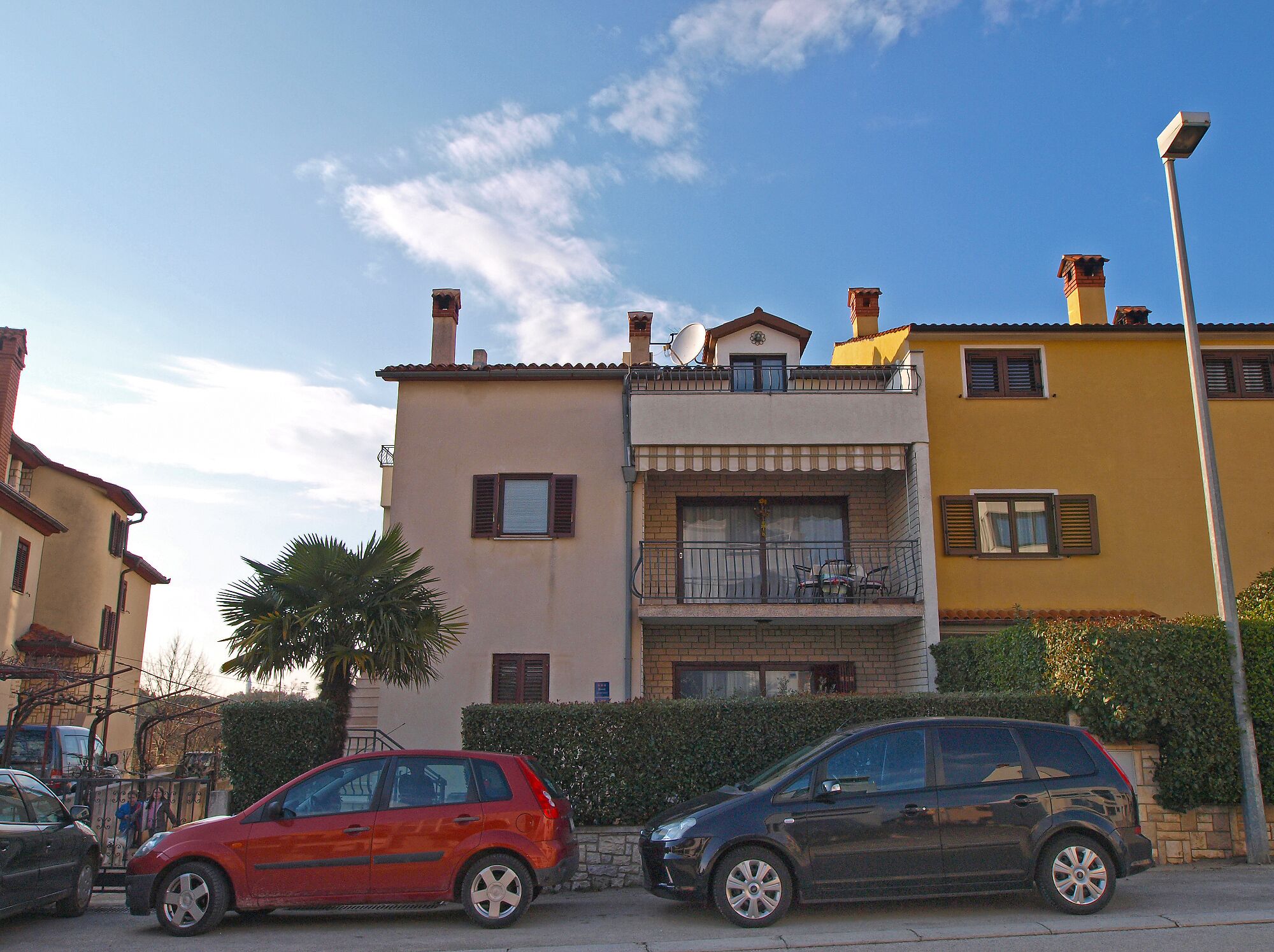 A multi-story building with balconies, a street lamp, and parked cars.