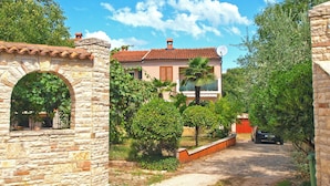 A stone archway leading to a house with a tiled roof, surrounded by greenery and a gravel path. - Apartment 1049/3911 (Istria - Rovinj), 1300m from the beach (Rovinj)