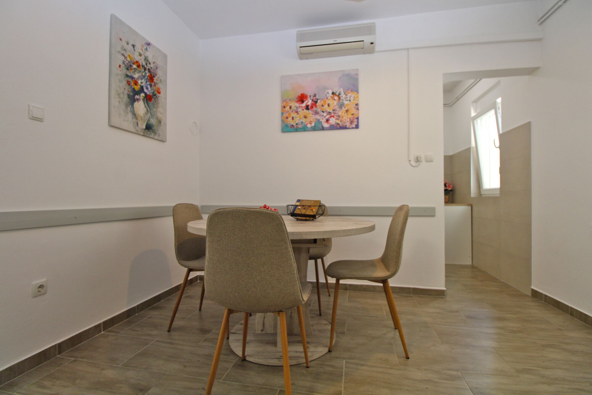 A dining area with a round table, four chairs, and two floral paintings on the walls.