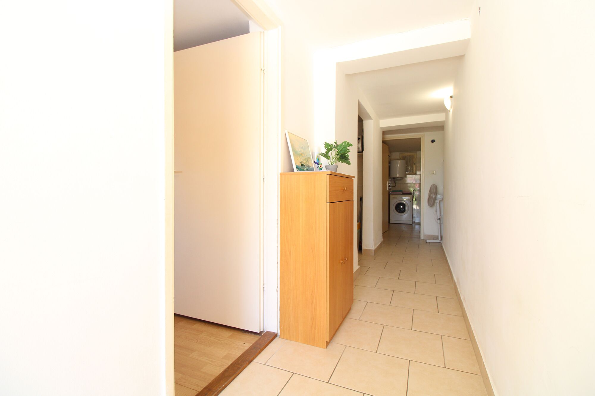 Ein Flur mit einem Holzschrank, einer Waschmaschine und einem Fliesenboden.