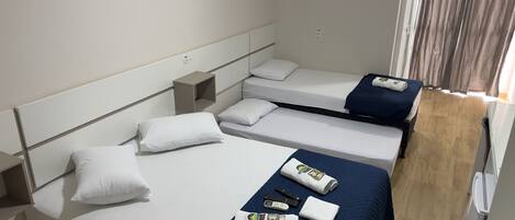 Une chambre d’hôtel avec deux lits simples, une petite table de chevet, une commode et une fenêtre avec des rideaux.