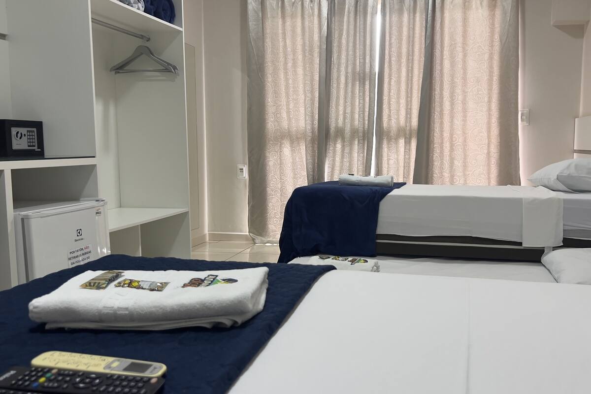 Une chambre d’hôtel avec deux lits, une armoire, un bureau avec un ordinateur et une fenêtre avec des rideaux.