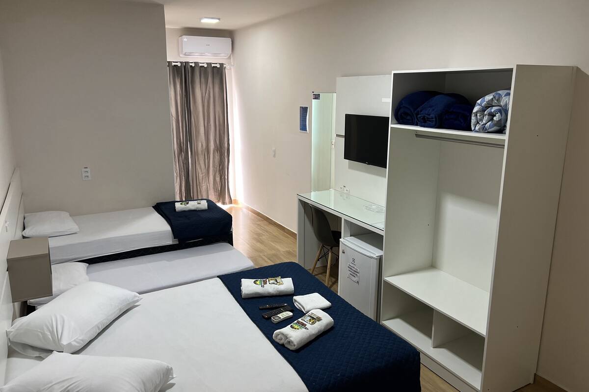 Une chambre d’hôtel avec deux lits simples, un bureau avec une télévision, une armoire et une petite kitchenette.