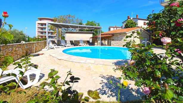 A swimming pool with lounge chairs, a stone wall, and a building in the background. - Apartment 1056/4401 (Istria - Pula), 500m from the beach (Pula)