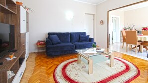 A living room with a blue sofa, a glass coffee table, a wooden TV stand, and a herringbone-patterned floor. - Apartment 1056/4401 (Istria - Pula), 500m from the beach (Pula)