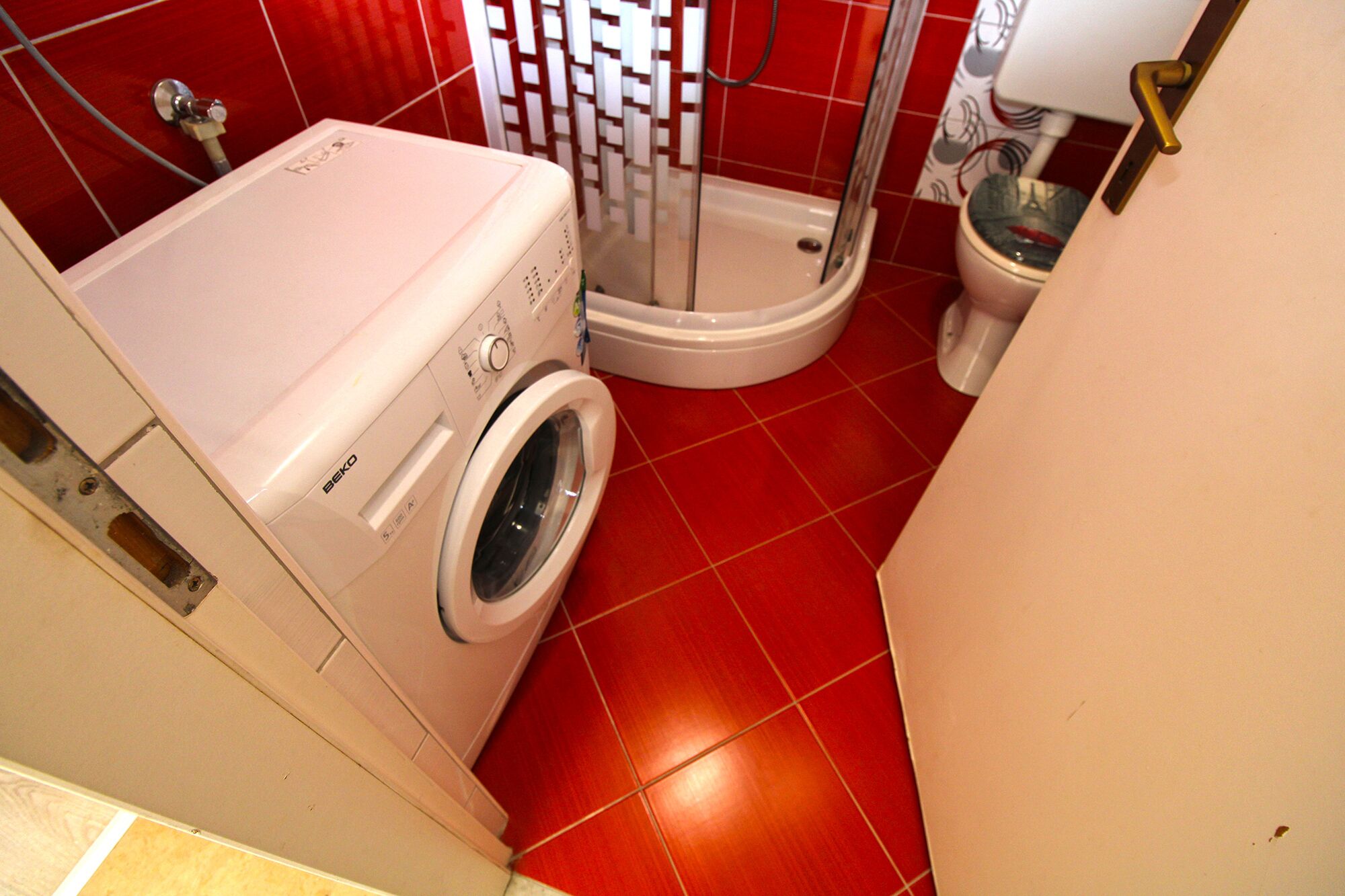 A compact bathroom with a washing machine, a shower, and a toilet.