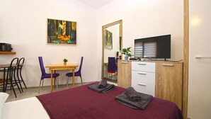 A hotel room with a bed, a desk with a chair, a television, a wardrobe, and a painting on the wall.