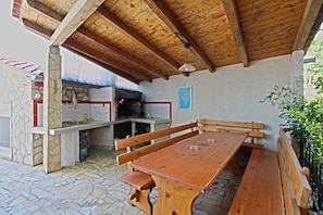 Una zona de cocina al aire libre con paredes de piedra, una mesa de madera y bancos.