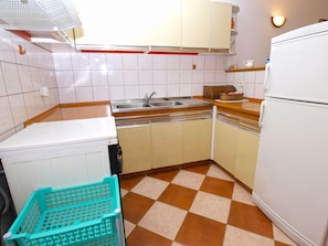 Compact kitchen with a refrigerator, sink, and wooden countertop, featuring a checkered tile floor and a convenient storage basket.