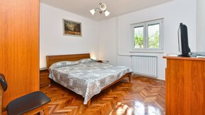 A bedroom with a wooden bed, a desk with a computer, a chair, a radiator, and a window with a view of greenery. - Apartment 1066/5084 (Istria - Rovinj), 1000m from the beach (Rovinj)