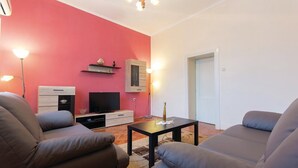 A living room with a red accent wall, a flat-screen TV, a small cabinet, a coffee table, and two armchairs.