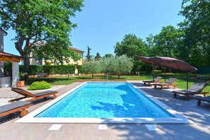 Relax by the rectangular pool surrounded by a paved deck and lounge chairs with umbrellas.