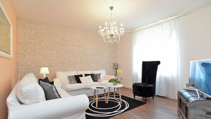 A modern living room with a white sofa, a black armchair, a round coffee table, a chandelier, and a vintage suitcase. - Apartment 1089/9537 (Istria - Poreč), 2000m from the beach (Poreč)