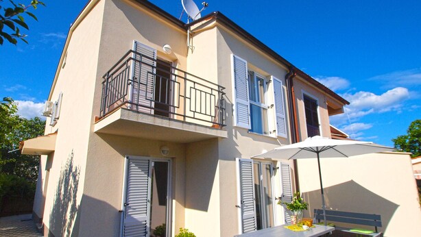 Un immeuble de deux étages doté d’un balcon, d’une antenne parabolique et d’une terrasse avec une table et des chaises.