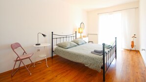 Une chambre à coucher avec un lit, une chaise, une table de chevet, une lampe et une fenêtre.