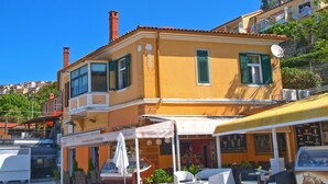 A yellow building with green shutters, a covered outdoor seating area, and a visible storefront. - Apartment 1093/9443 (Istria - Rabac), 100m from the beach (Rabac)
