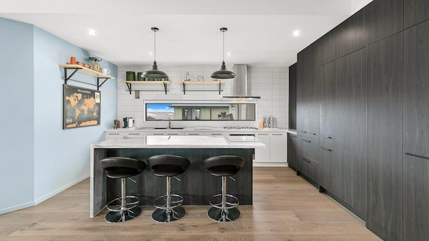 A modern kitchen with a central island, bar stools, pendant lighting, and a large window.