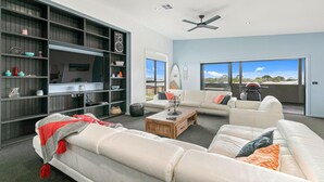 A spacious living room with a large bookshelf, a white sofa set, and a view of the outdoors.
